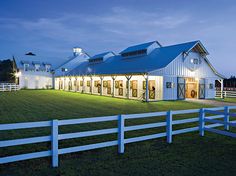 a large white barn sitting on top of a lush green field next to a white fence