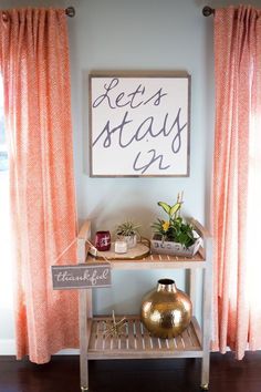 a sign that says let's stay next to a shelf with some plants on it