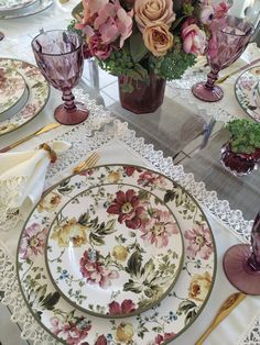 the table is set with pink and yellow flowers in glass vases, lace doily, and place settings