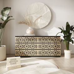 a white and black dresser sitting next to two potted plants