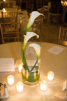 a vase filled with white flowers sitting on top of a table next to lit candles