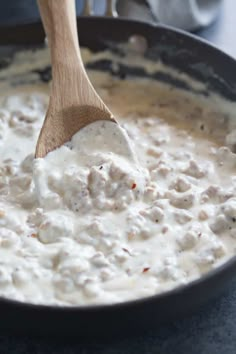 a wooden spoon in a skillet filled with white sauce and meatballs on the side