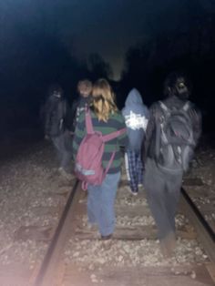 three people walking on train tracks in the dark with one person carrying a pink backpack