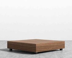 a square wooden table sitting on top of a cement floor next to a white wall