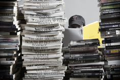 there is a stack of newspapers and a hat on top of the bookshelf