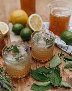 three glasses filled with lemonade and mint on top of a wooden table next to lemons