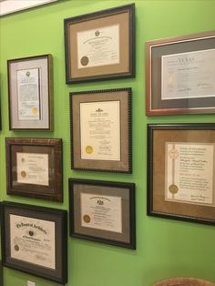 many framed diplomas are on the wall in front of a green wall with pictures