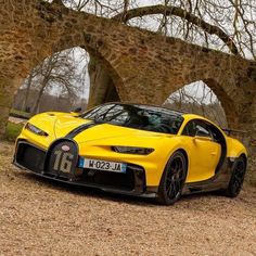 a yellow sports car parked in front of an old stone bridge with trees and grass