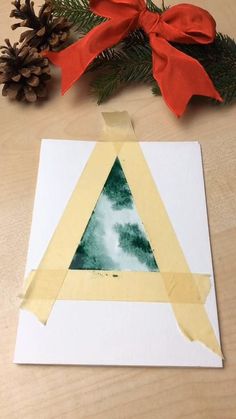 an origami triangle with a red bow and pine cones on the table next to it