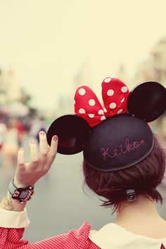 a woman wearing a minnie mouse hat with her hand up to her ear and the word mickey written on it