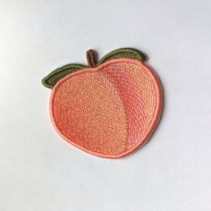 an embroidered peach patch with two green leaves on the top and one orange in the middle