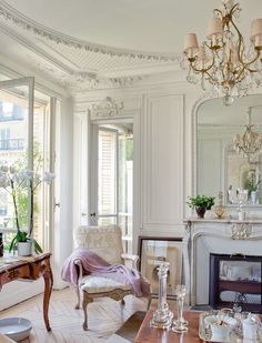 a living room filled with furniture and a chandelier hanging from the ceiling next to a fire place