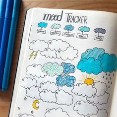 an open notebook with weather and clouds on it next to two blue pencils,