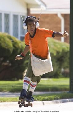 a young man riding a skateboard down a street wearing headphones and carrying a bag