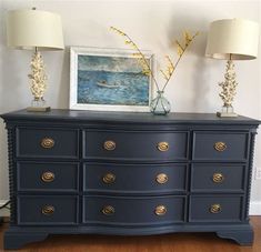 a blue dresser with two lamps and a painting on the wall in front of it