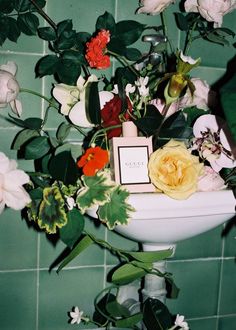 a white sink sitting next to a green tiled wall with flowers on top of it