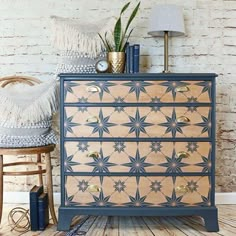 a blue and gold chest of drawers next to a chair with a plant on top