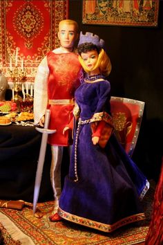 two dolls standing next to each other in front of a table