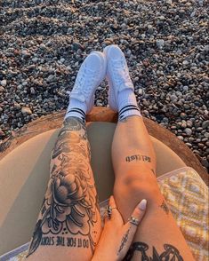 a person with tattoos on their legs sitting on a surfboard in front of the ocean