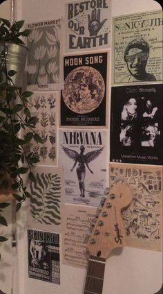 a guitar is hanging on the wall next to some posters and a potted plant