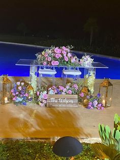 a table with flowers and candles on it next to a swimming pool at night time