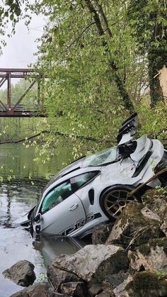 a car that has been flipped over in the water near a bridge and some rocks