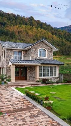 a large house in the middle of a lush green field with mountains in the background