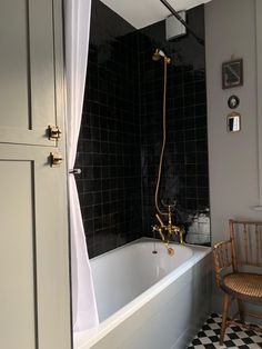 a black and white tiled bathroom with an old fashioned bathtub, shower head, and chair