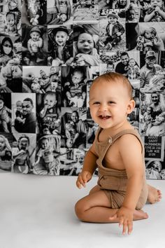 a baby sitting on the floor in front of a wall with many pictures behind it