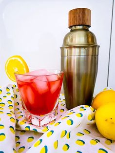 a drink in a glass next to some lemons and a shaker