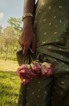 a person holding flowers in their hands on the grass with trees in the back ground