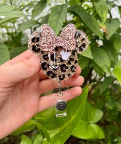 a hand holding a mickey mouse brooch with pink and black sequins on it