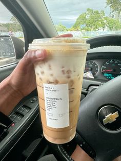 a person holding up a cup of iced coffee in their car with the steering wheel behind them