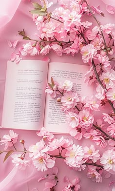 an open book sitting on top of pink flowers