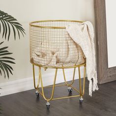 a basket with wheels on the floor next to a potted plant and a blanket