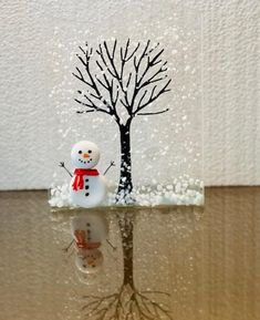 a snowman is standing in the water next to a tree with no leaves on it