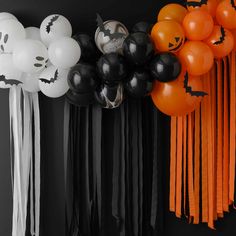 halloween decorations and balloons are hanging on the wall in front of a black backdrop with white, orange and black balloons