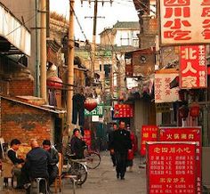 people are walking down an alley way with signs on the buildings and bicycles parked in front of them