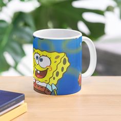 a blue and yellow coffee mug sitting on top of a wooden table next to a book