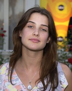 a woman with long brown hair wearing a floral shirt and looking off into the distance