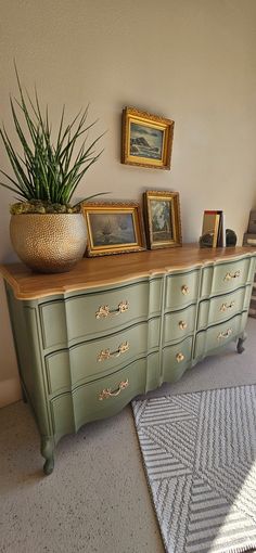 a green dresser with pictures on it and a potted plant