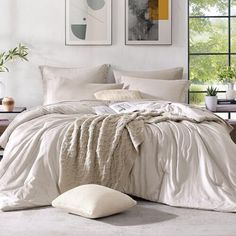 a bed with white sheets and pillows in a room next to two pictures on the wall