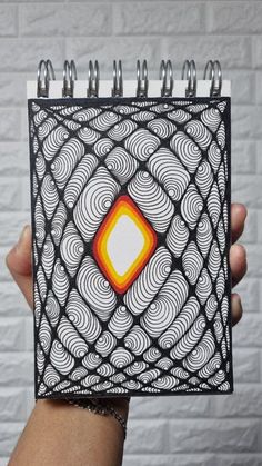 a hand holding up a spiral notebook with an orange and white design on it