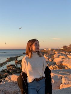 a woman is standing on the rocks near the water and looking off into the distance