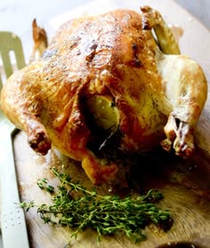 a whole chicken on a cutting board next to a knife and fork