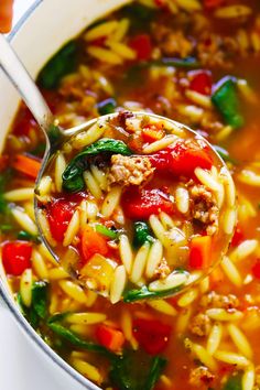 a ladle full of pasta soup with meat and veggies in it is being held by a spoon