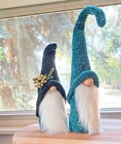 two knitted gnomes sitting on top of a wooden table next to a window