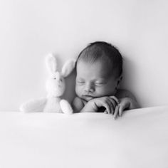 a baby sleeping next to a stuffed animal on top of a white sheet in black and white