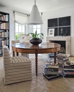 a dining room table surrounded by chairs and books in front of a fire place with a potted plant on top