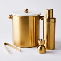 a gold canister with two cups next to it and a pair of tongs